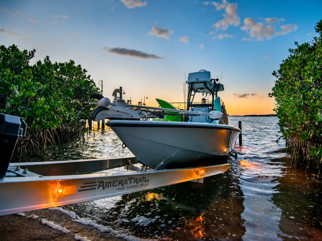Center-console fishing boat launching at sunset on an Amera Trail aluminum boat trailer between mangroves.